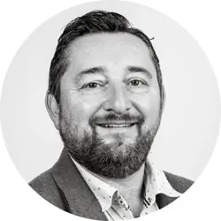 Andrew Rigby. Andrew is a white man with short dark hair and a short beard. He is wearing an informal blazer and an open-necked collared shirt.