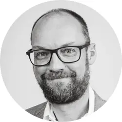 Scott Payton. Scott is a white man with very short dark hair and a short beard. He is wearing glasses, a light jacket and collared shirt.