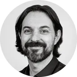 Tom Golden. Tom is a white man with collar-length swept back dark hair and a short beard. He is wearing a dark shirt.